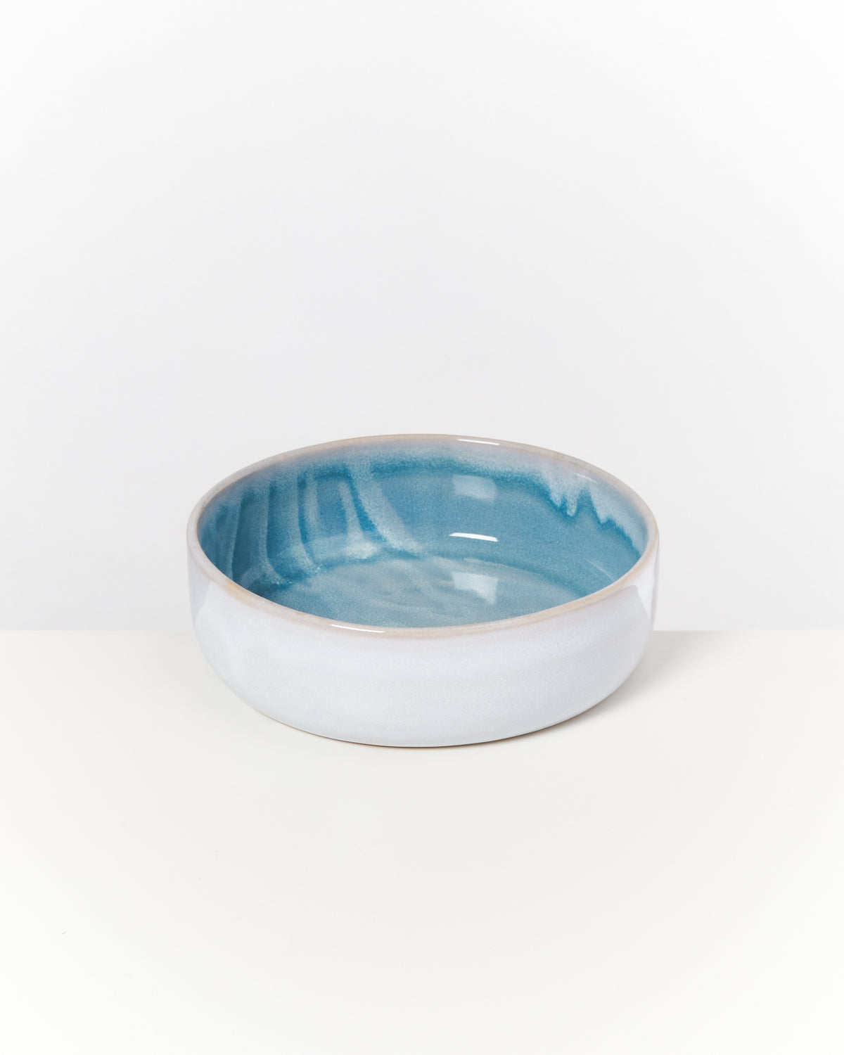 Keramikschüssel mit blauer Innenseite und weißer Außenseite, auf einer weißen Fläche platziert.