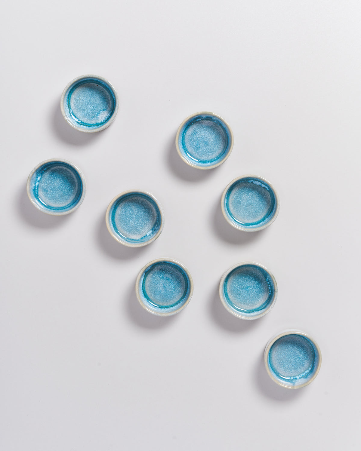 Acht kleine, runde Schalen mit blauer Glasur auf weißem Hintergrund.