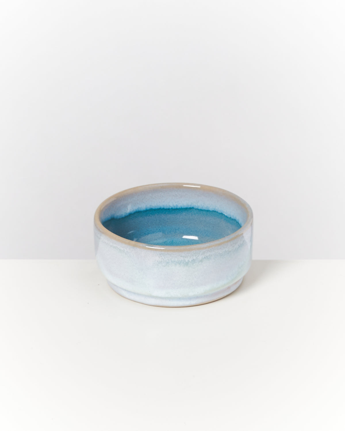Eine flache, blau-weiß glasierte Keramikschale steht auf einer weißen Oberfläche.
