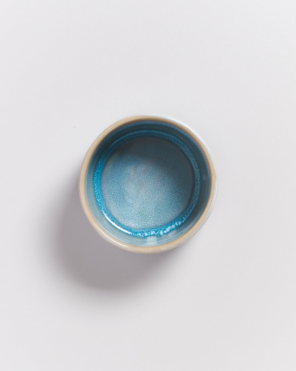 Keramikschale mit blau-grünem Inneren auf weißem Hintergrund.