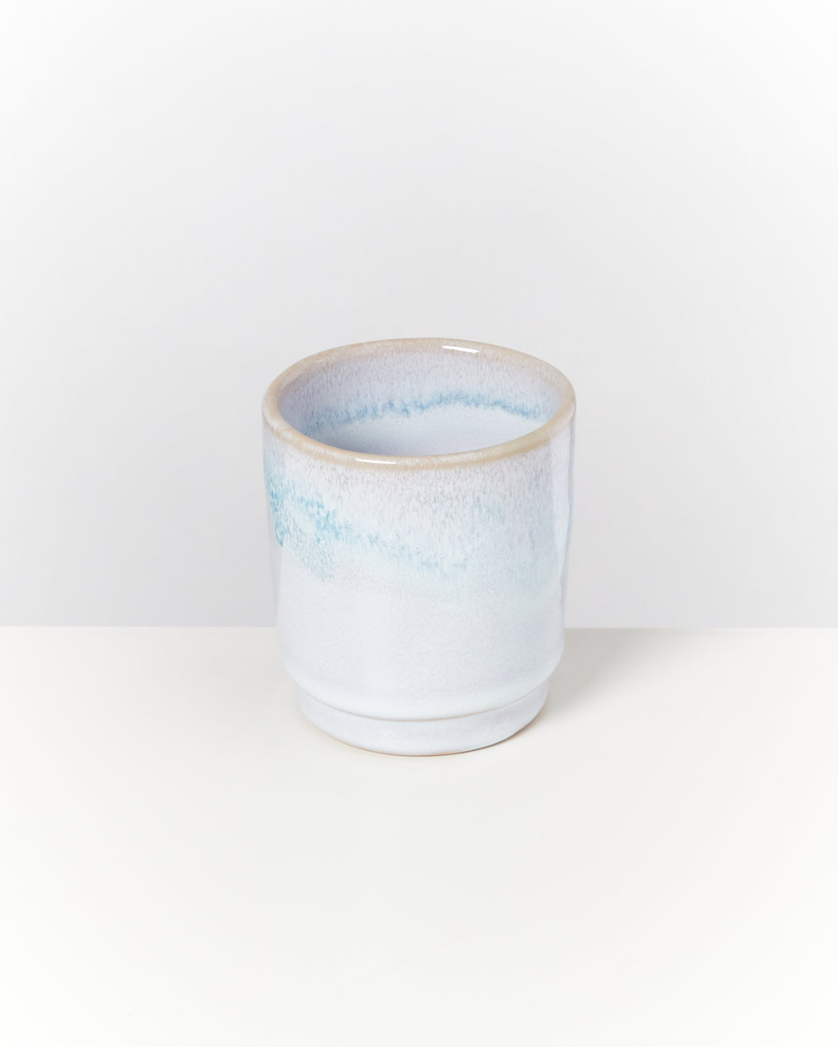 Keramiktasse mit blau-weißer Glasur auf einem weißen Hintergrund.