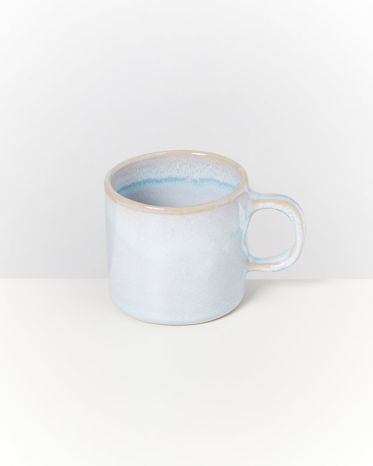 Keramiktasse in hellem Blau und Beige auf weißem Hintergrund.