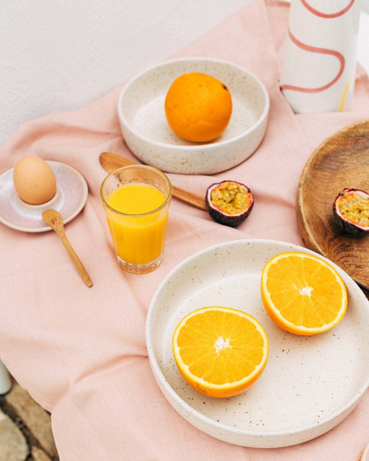 Ein Tisch mit einem Ei, einem Glas Orangensaft, einer Orange, einer offenen Passionsfrucht und Orangenhälften auf Tellern.
