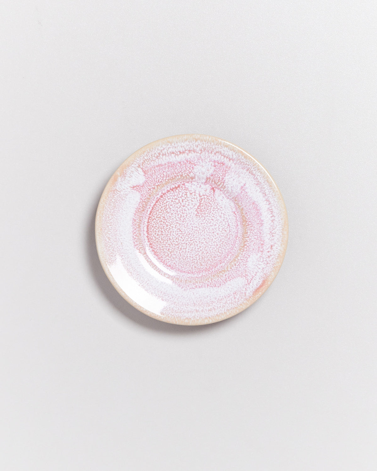 Runder Teller mit rosa und weißen Mustern auf einer neutralen, hellen Oberfläche.