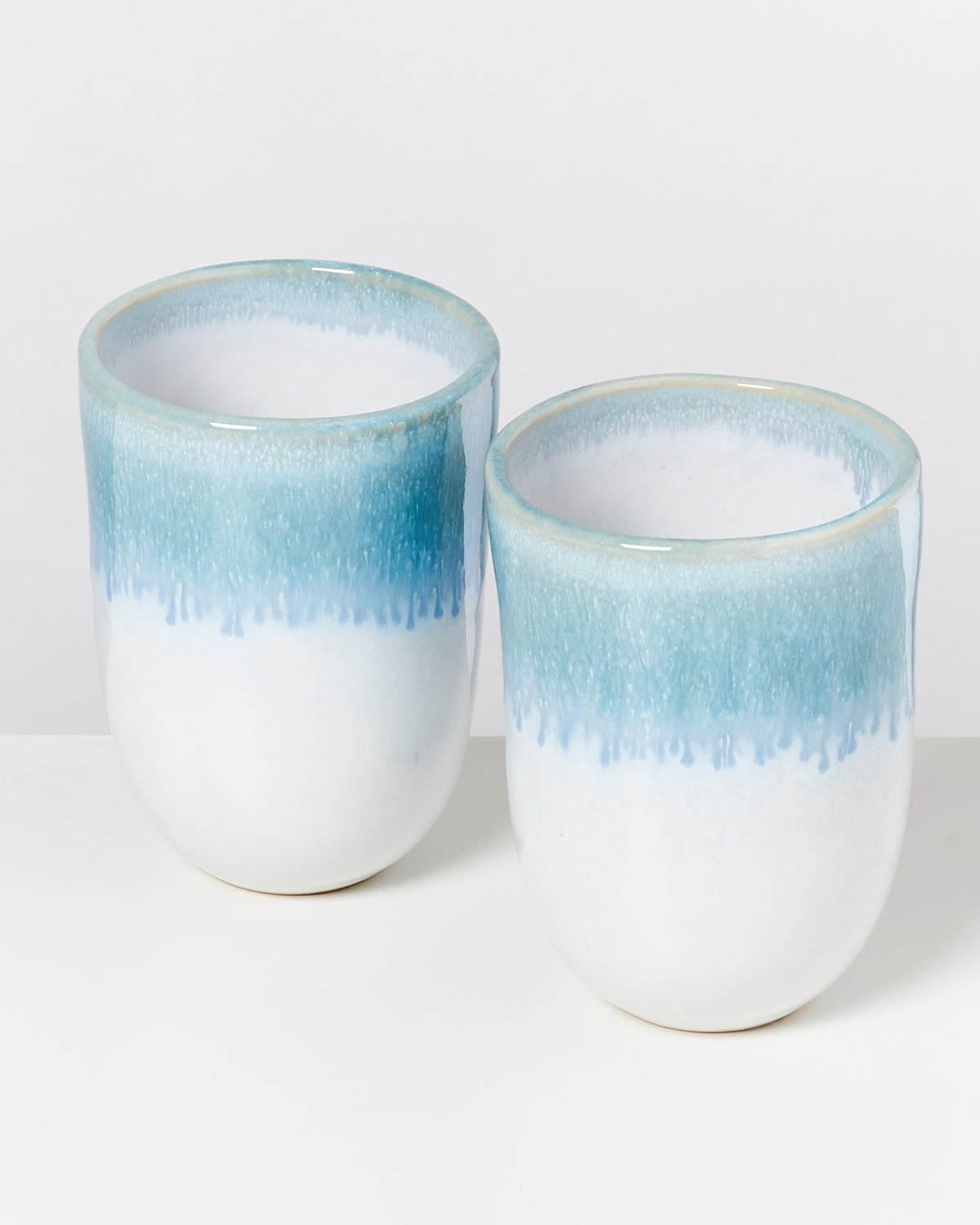 Zwei weiße Keramiktassen mit blauem Farbverlauf oben auf einem weißen Hintergrund.