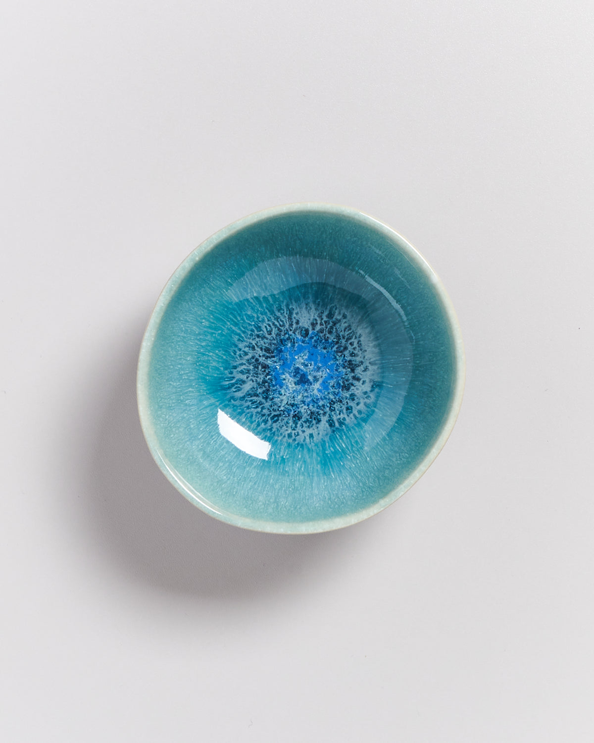 Kleine, runde, blaue Schale mit kunstvoll bemaltem, abstraktem Muster auf weißem Hintergrund.