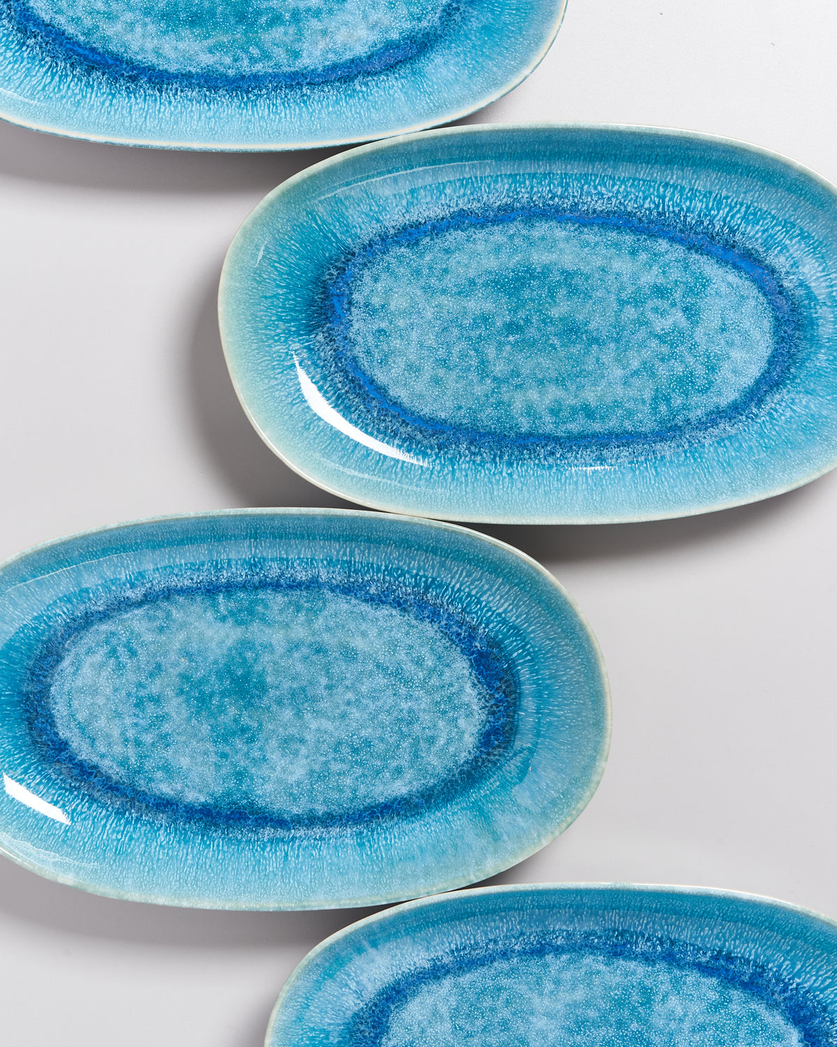 Vier ovale, blaue Teller mit einem aquarellähnlichen Design liegen auf einer weißen Oberfläche.