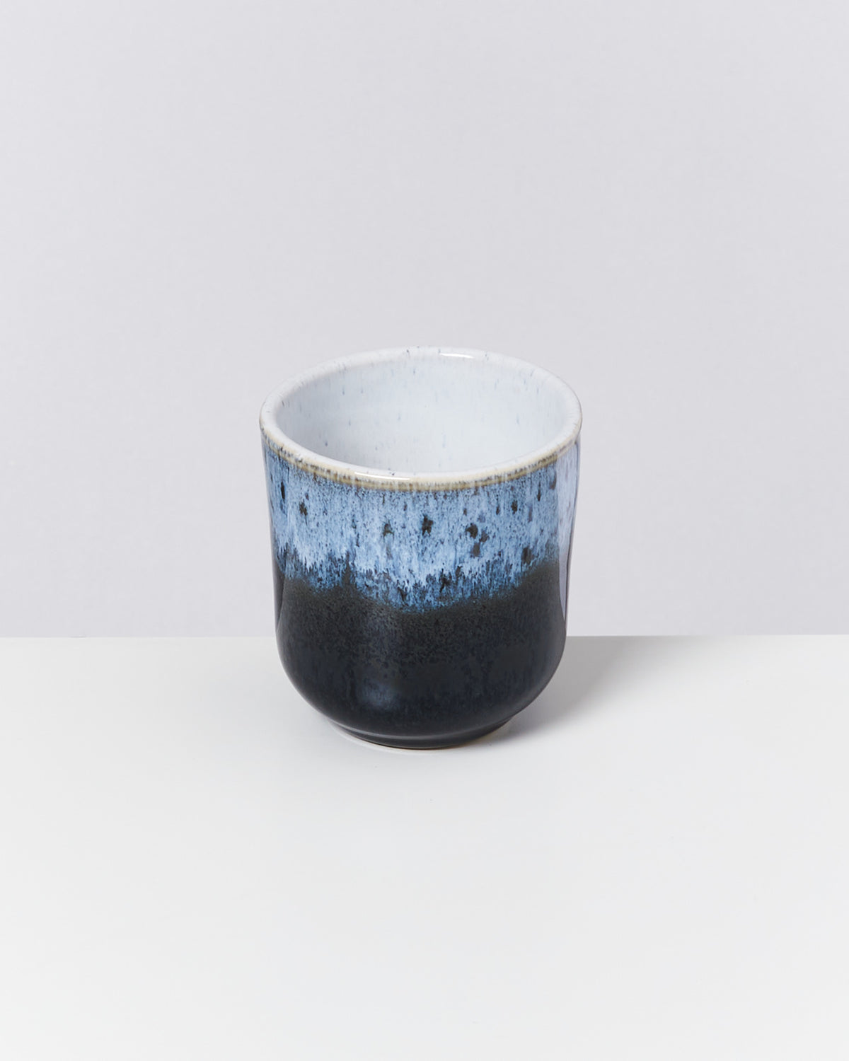 Keramikbecher mit blau-schwarzer Glasur auf hellem Hintergrund.