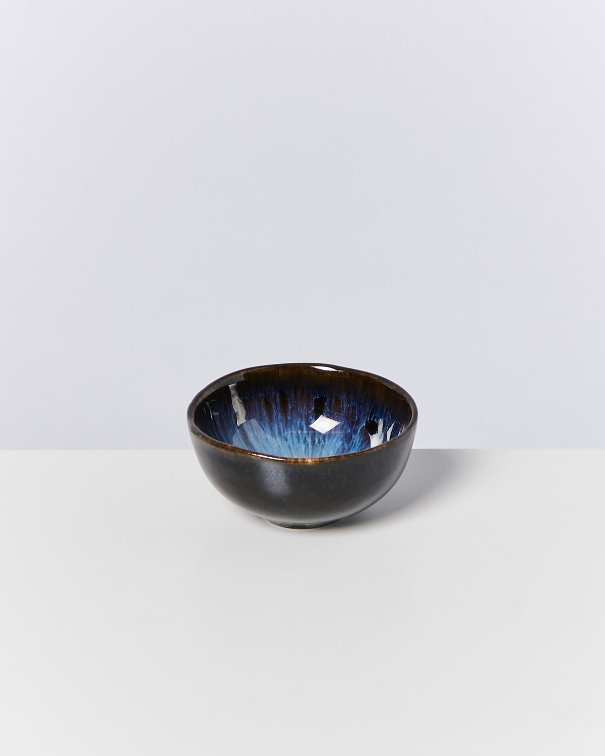 Keramikschale mit blau-weißer Glasur innen und dunkler Außenseite auf weißem Untergrund.