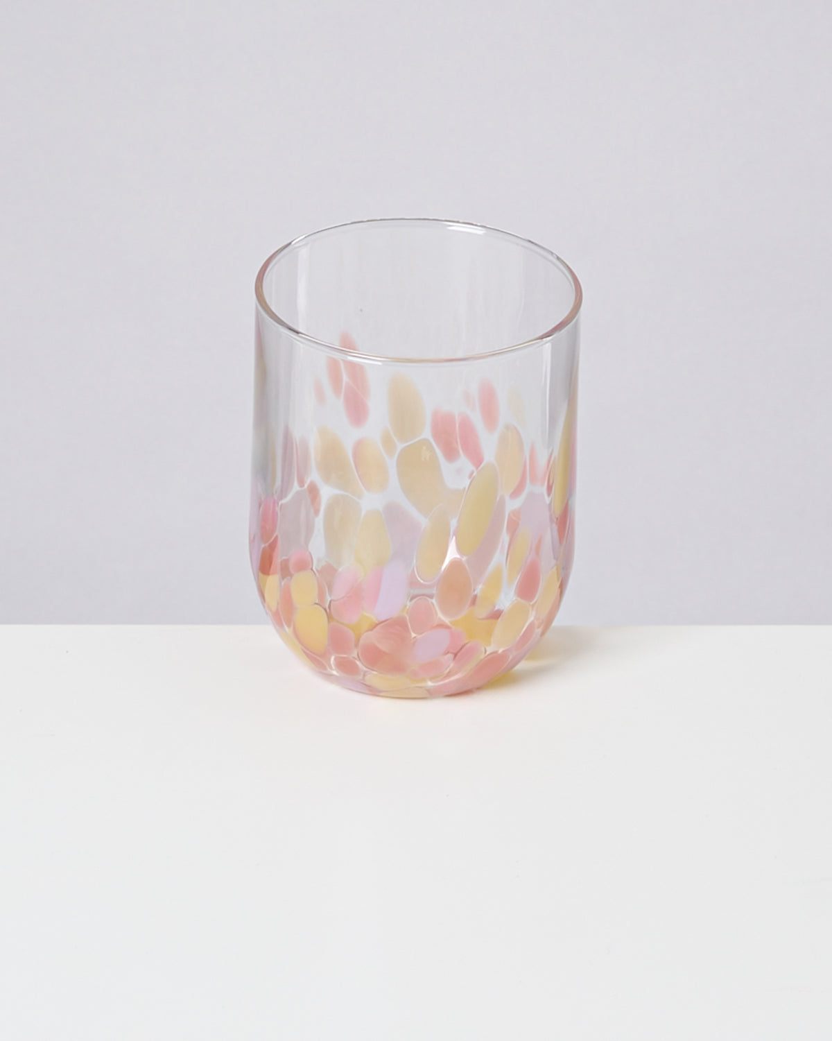 Ein Glas mit bunten Punkten in Rosa und Gelb steht auf einem weißen Tisch vor einem neutralen Hintergrund.