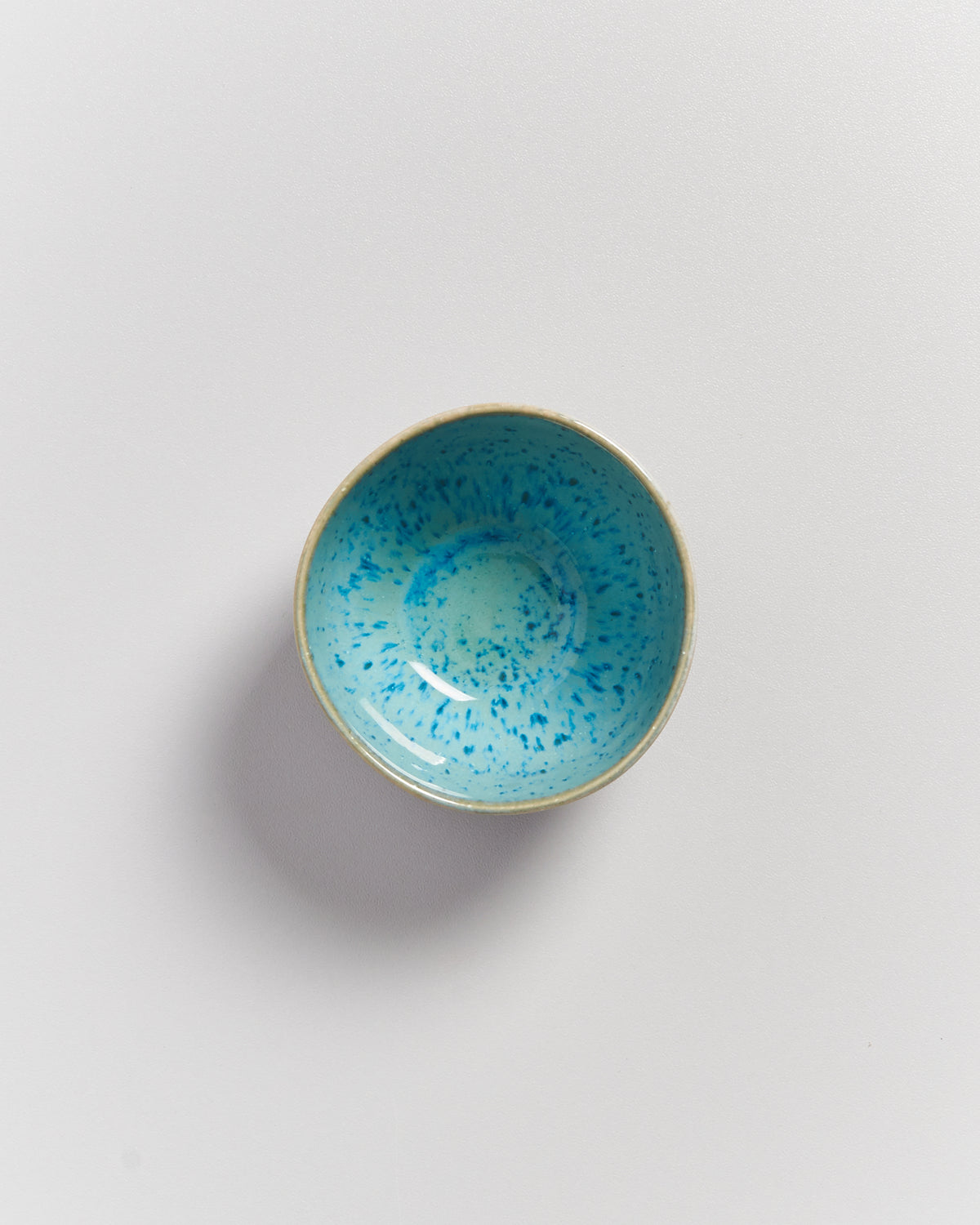 Schale mit türkis-blauem Muster auf weißem Hintergrund von oben fotografiert.