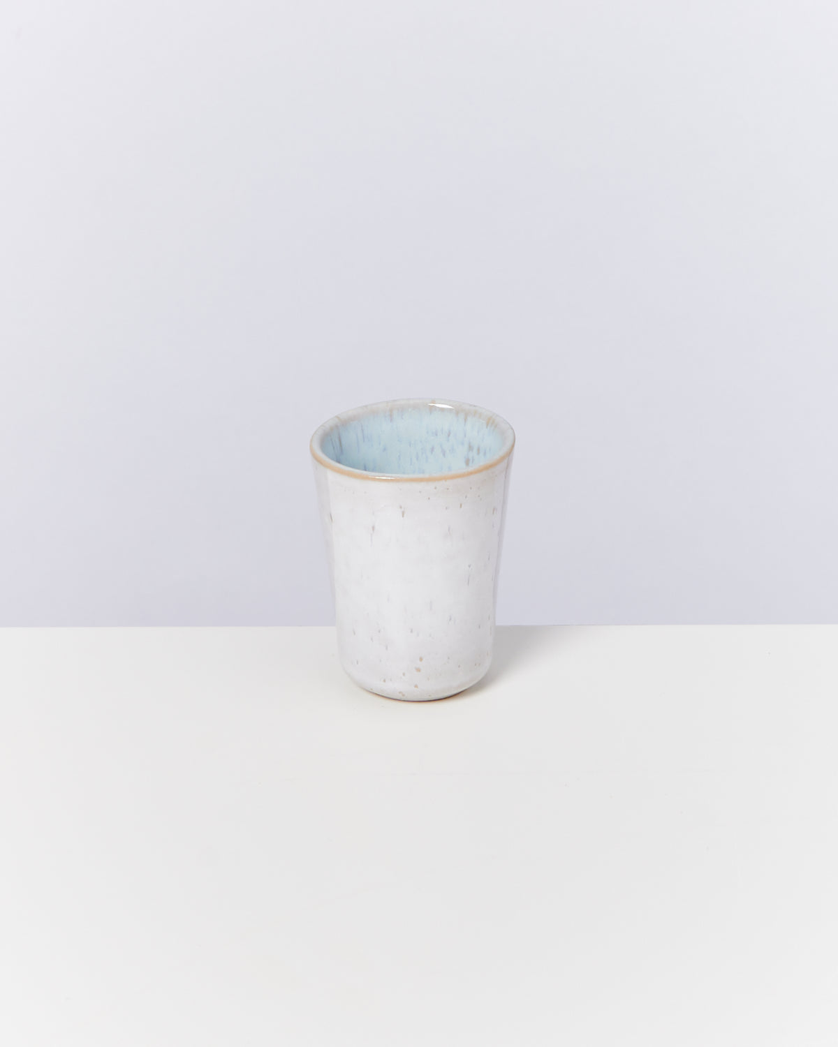 Ein weißer Keramikbecher mit hellblauer Innenseite steht auf einem weißen Hintergrund.