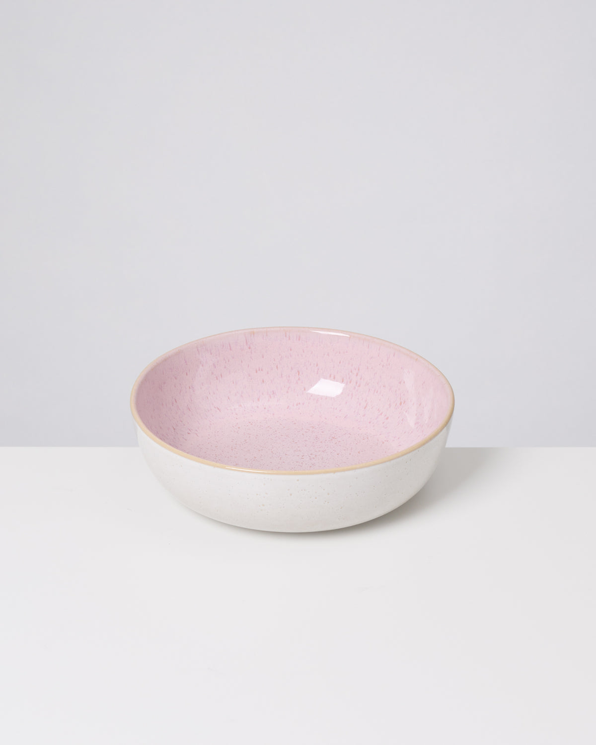 Weiße Schale mit rosa Innenfläche steht auf einem weißen Tisch vor grauem Hintergrund.