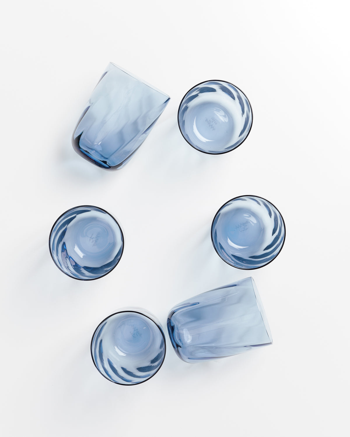 Sechs blaue Gläser, aus verschiedenen Winkeln fotografiert, liegen auf einer weißen Oberfläche.