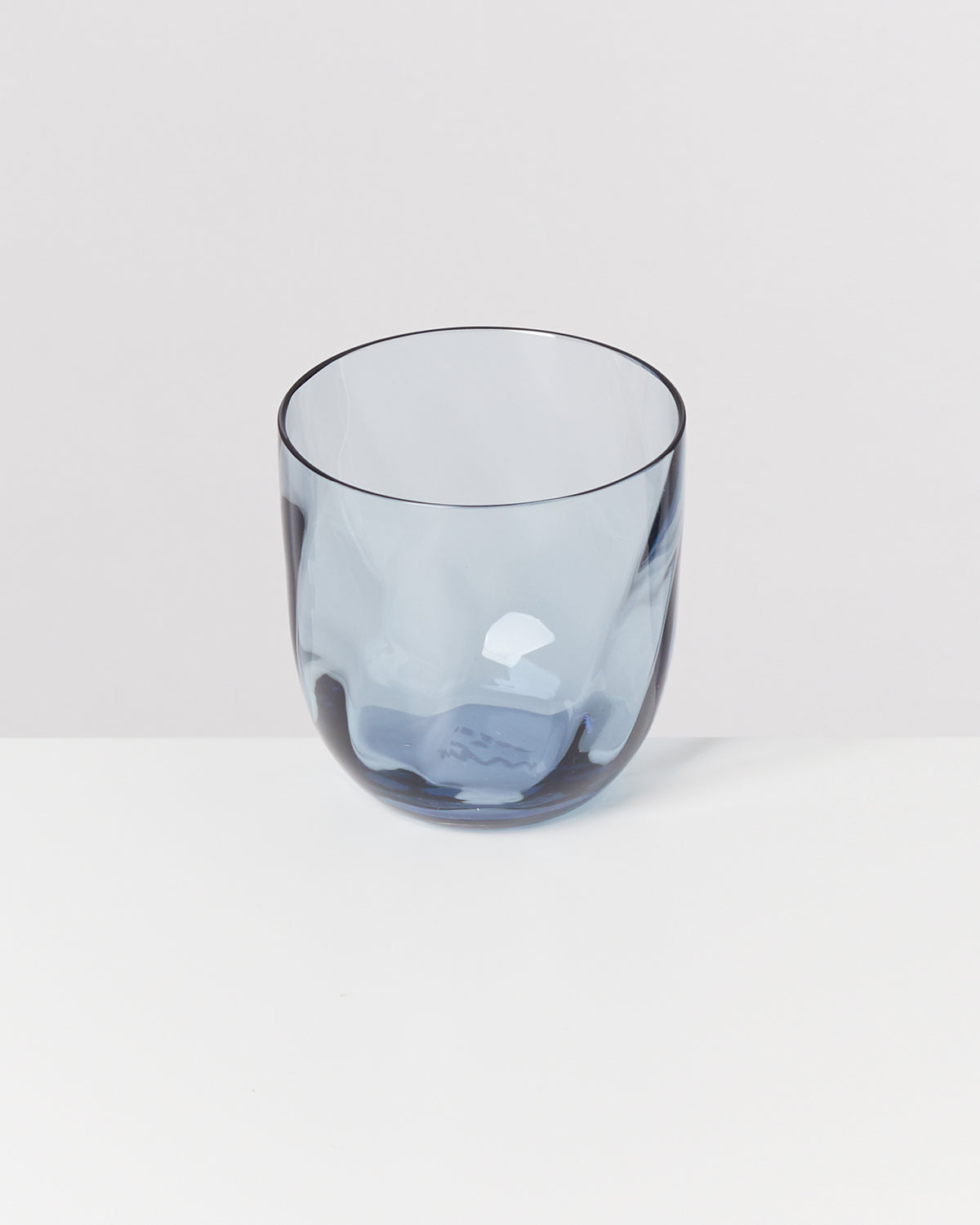 Ein durchsichtiges, blau getöntes Glas auf einem weißen Tisch vor einem grauen Hintergrund.
