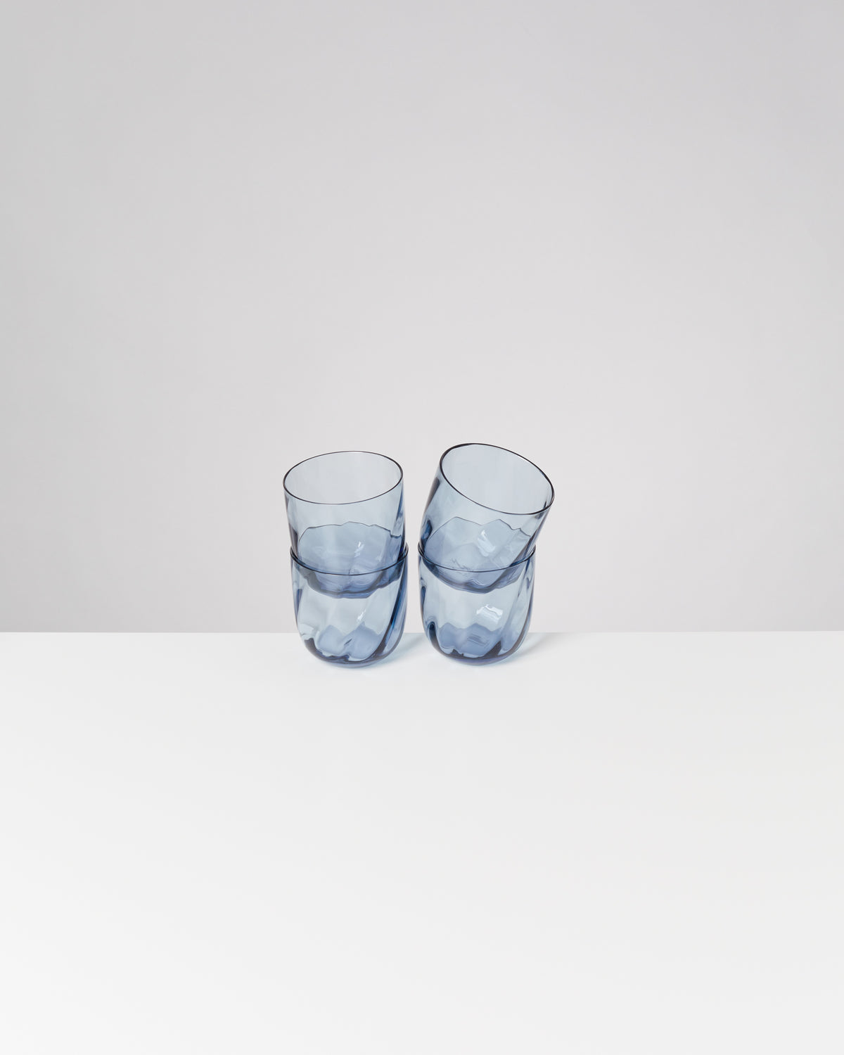 Zwei blaue, ineinander verschachtelte Trinkgläser stehen auf einem weißen Tisch vor einem grauen Hintergrund.