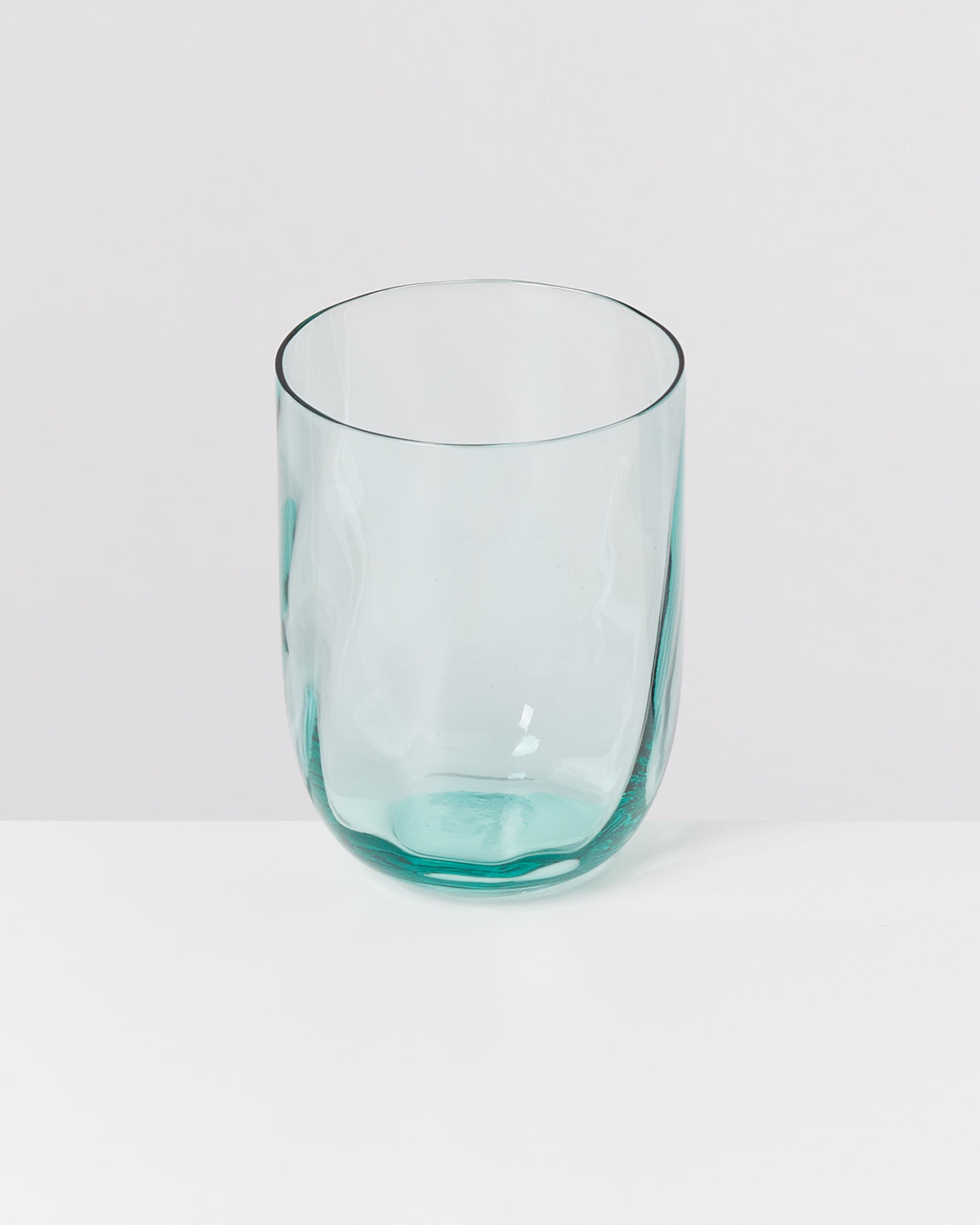 Ein durchsichtiges, bläuliches Glas steht auf einer weißen Oberfläche.