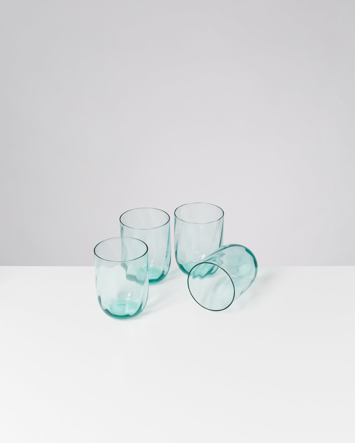 Vier türkisfarbene Trinkgläser auf einem weißen Tisch, eines davon liegt auf der Seite.