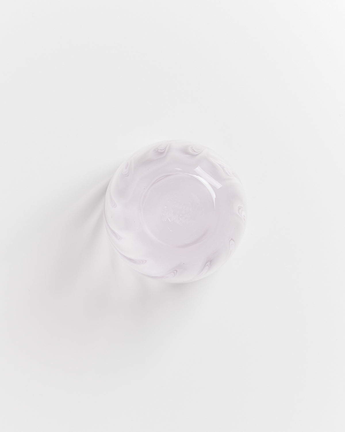 Runde, milchig-rosa Glasschale mit wellenförmigem Rand auf weißem Hintergrund, von oben fotografiert.
