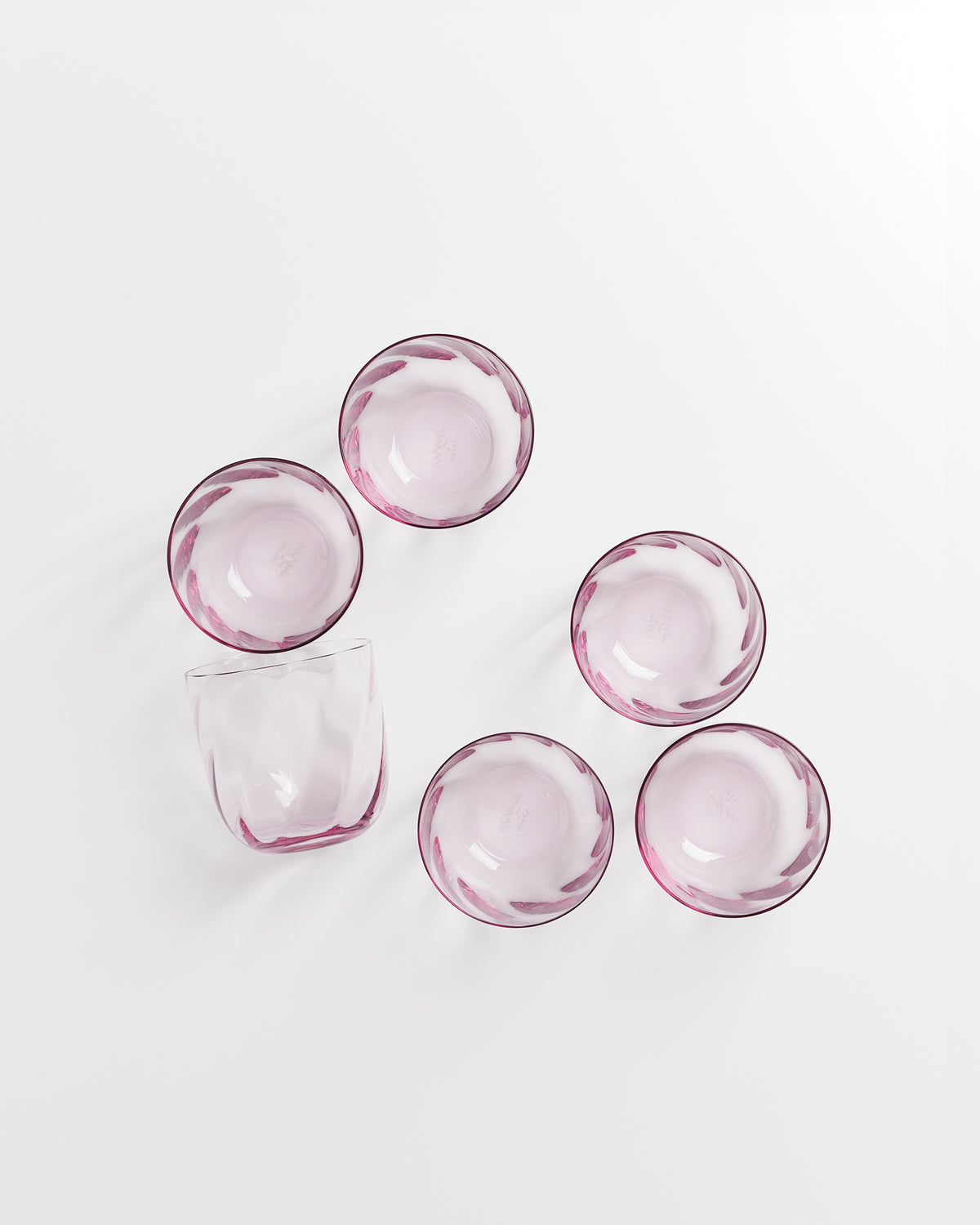 Sechs rosafarbene Glasschalen und ein Glas auf weißem Hintergrund.