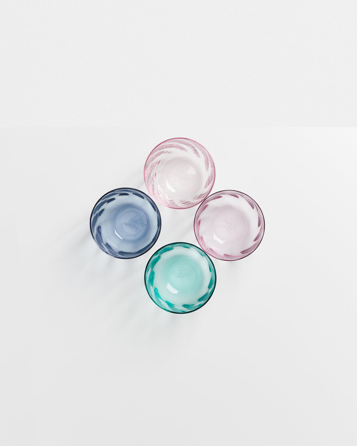 Vier bunte Glasschalen (blau, grün, rosa, lila) liegen auf einer weißen Oberfläche.