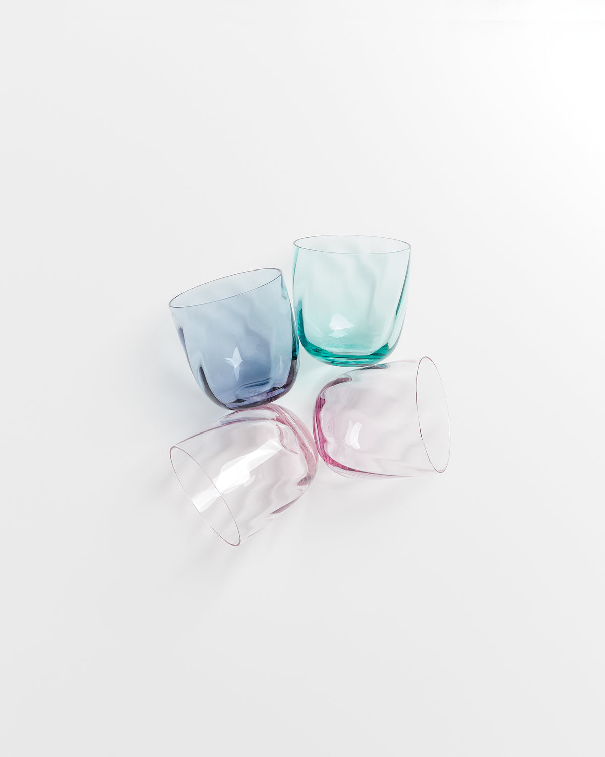 Vier bunte Glasbecher liegen umgedreht auf einem weißen Hintergrund.
