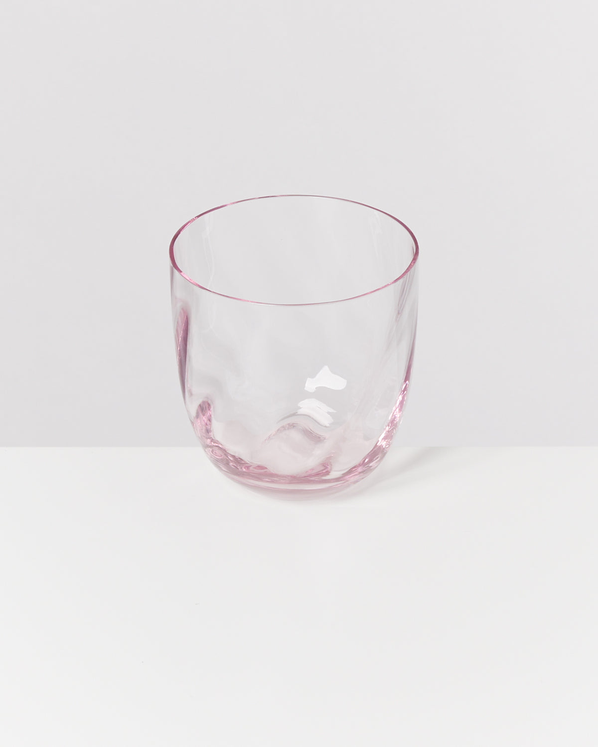 Ein durchsichtiges Glas mit einem rosafarbenen Rand steht auf einer weißen Oberfläche.