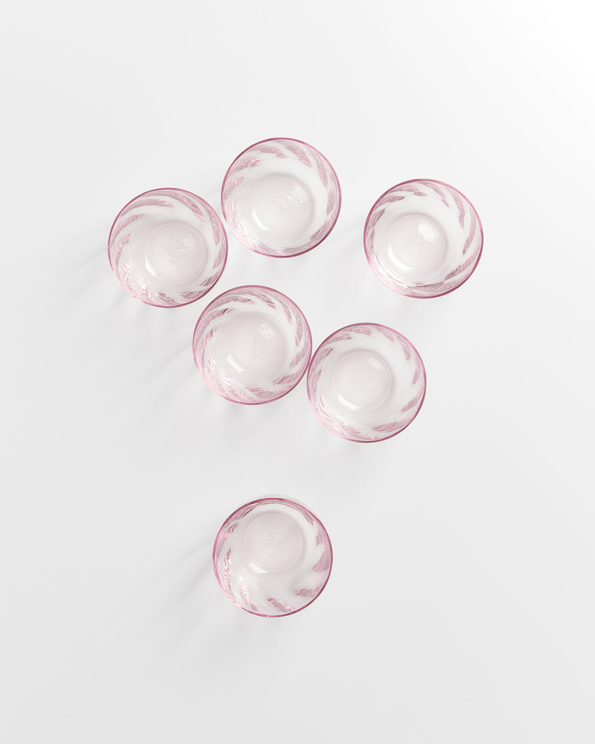 Sechs rosa Glasbecher mit dekorativen Mustern, von oben betrachtet, auf einer weißen Oberfläche angeordnet.