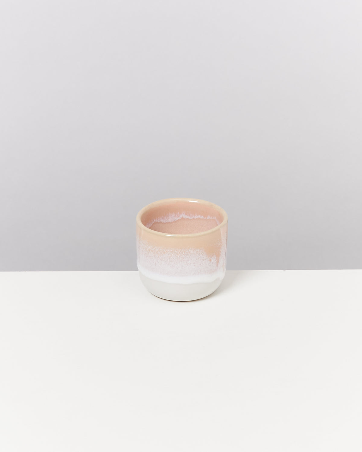 Kleine, zweifarbige Keramikschale in Rosa und Weiß auf einem weißen Tisch vor grauem Hintergrund.