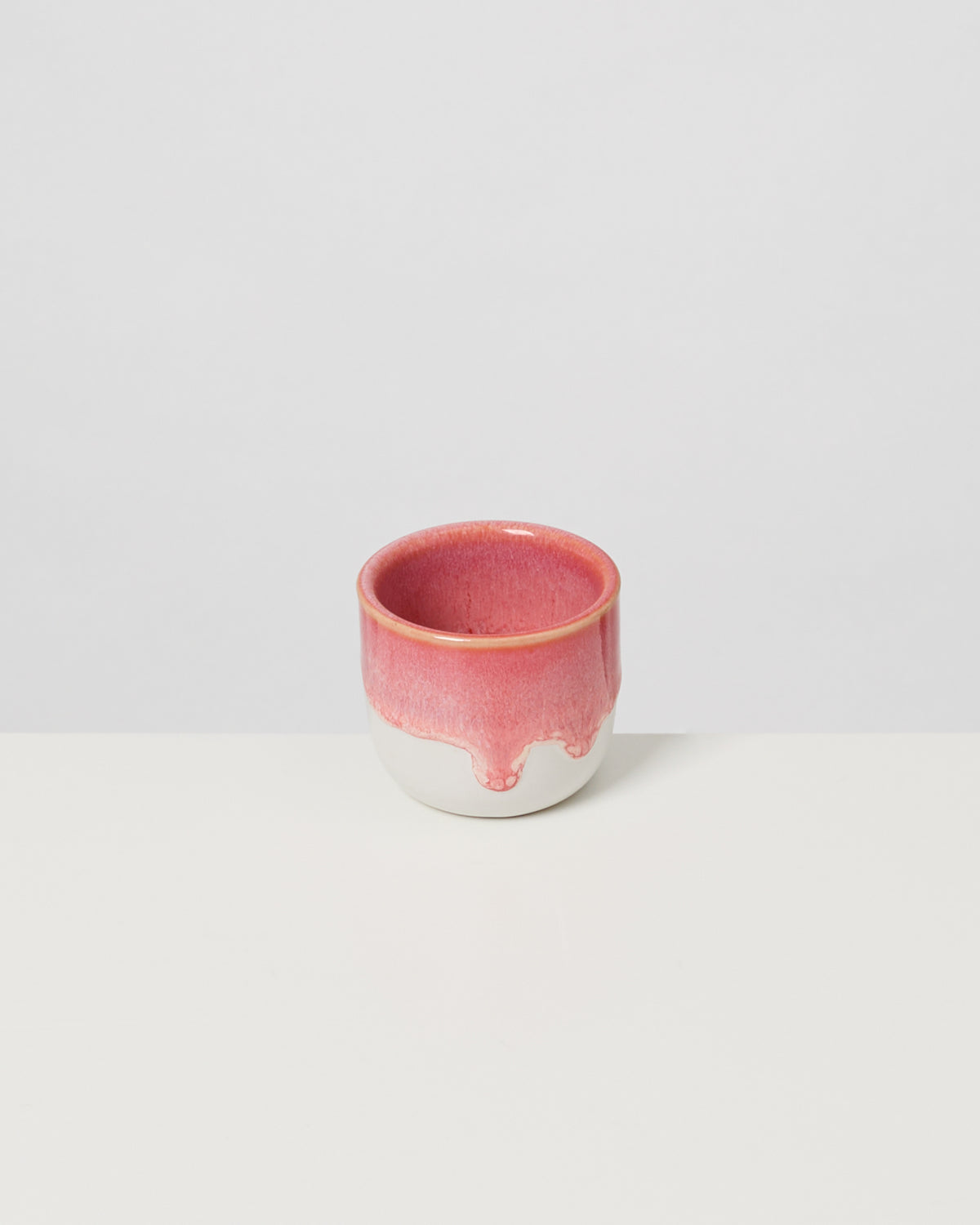 Kleiner weißer Becher mit rotem Verlaufsglasur, auf einem weißen Hintergrund.