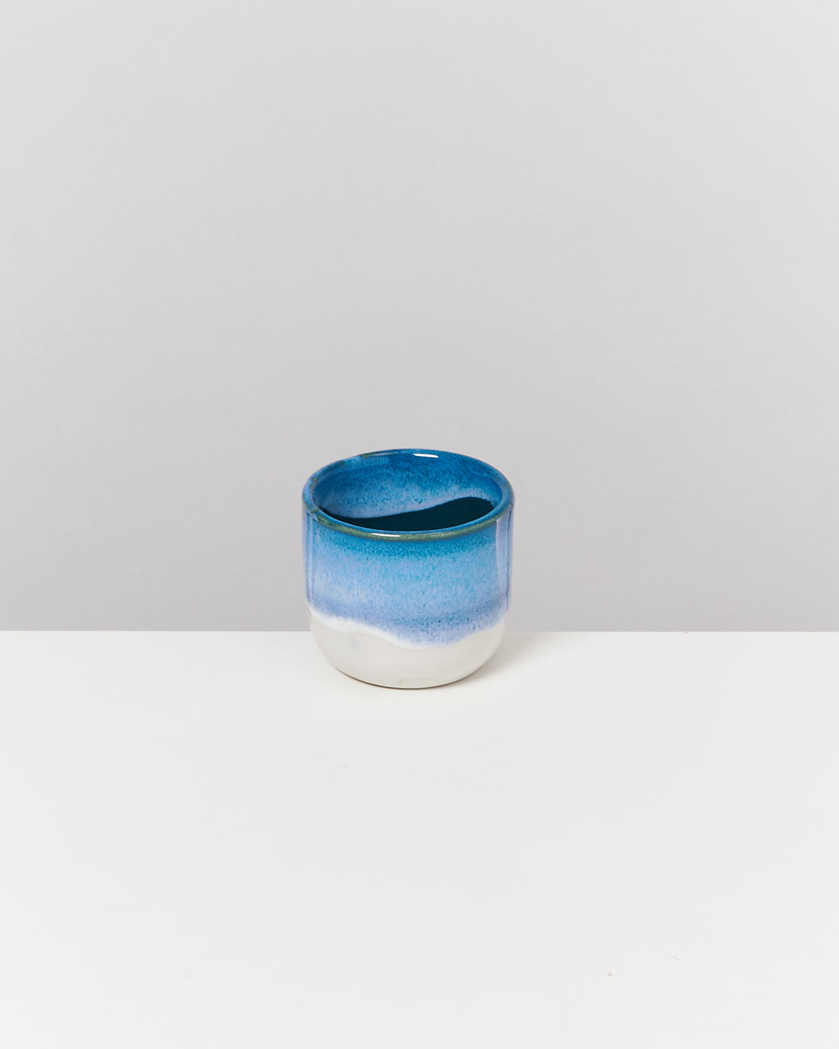 Ein blau-weißer Keramikbecher steht auf einer weißen Oberfläche vor einem grauen Hintergrund.