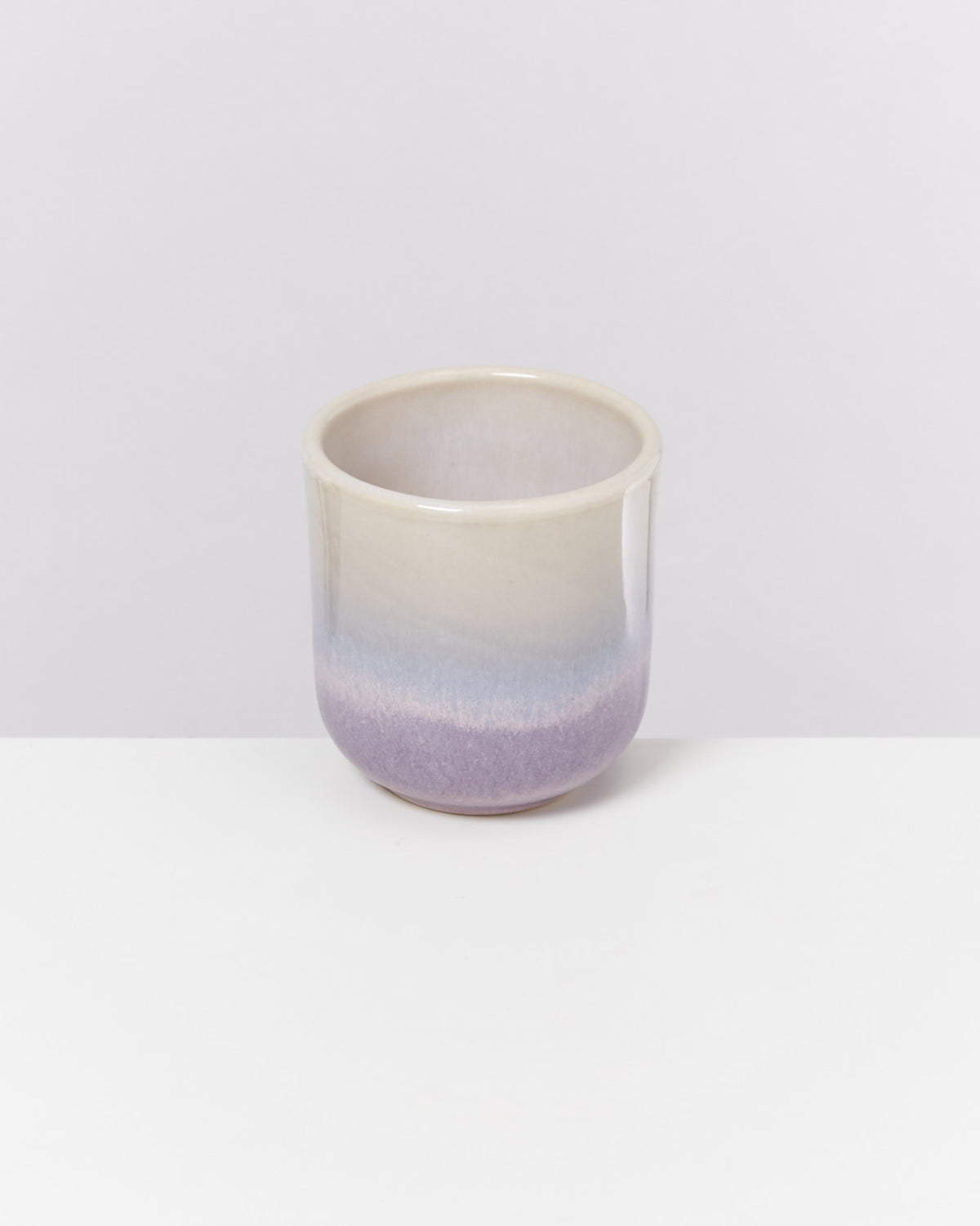 Keramikbecher mit Farbverlauf in Beige, Blau und Lila auf weißem Hintergrund.