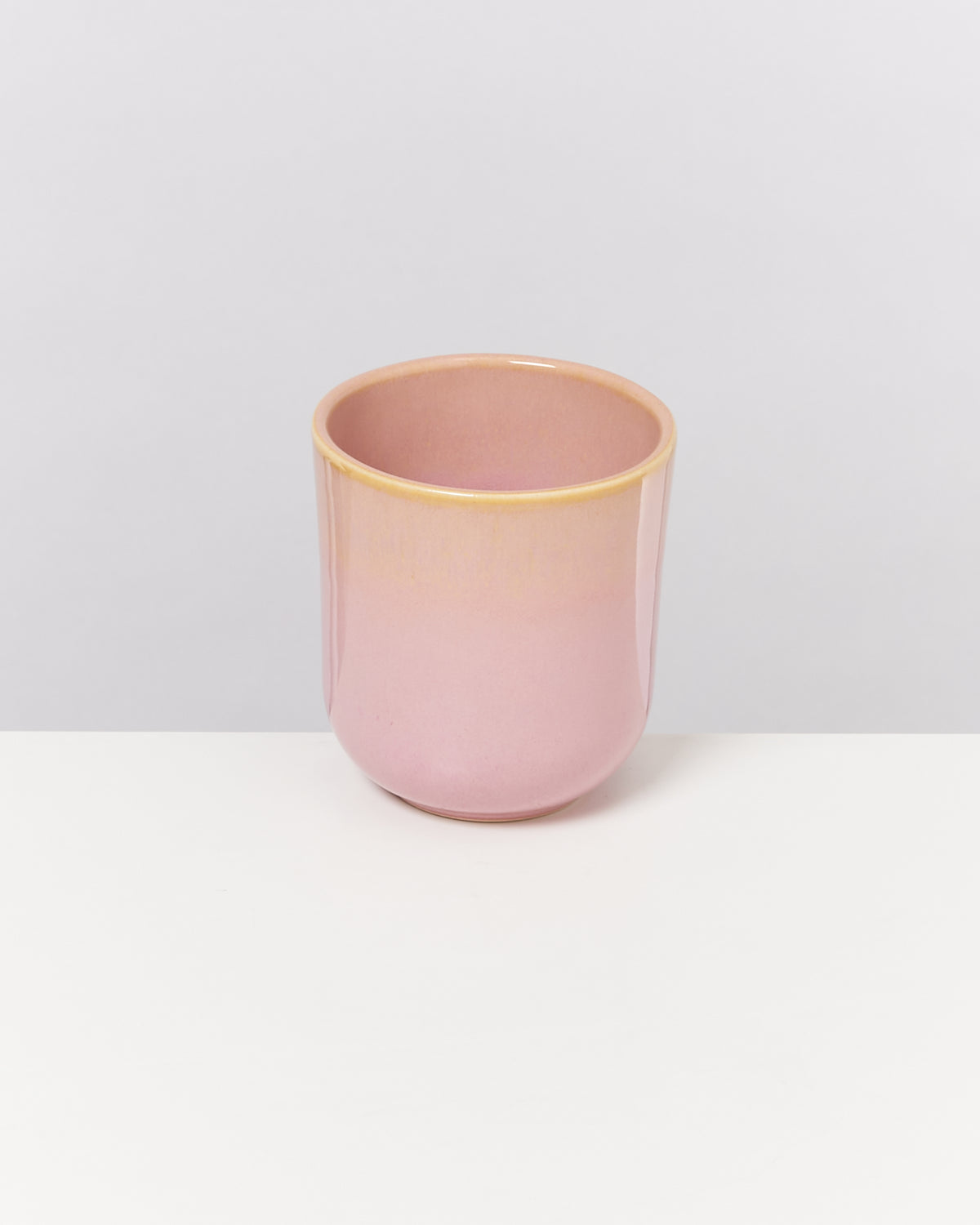 Rosa Keramikbecher auf einem weißen Tisch vor neutralem Hintergrund.