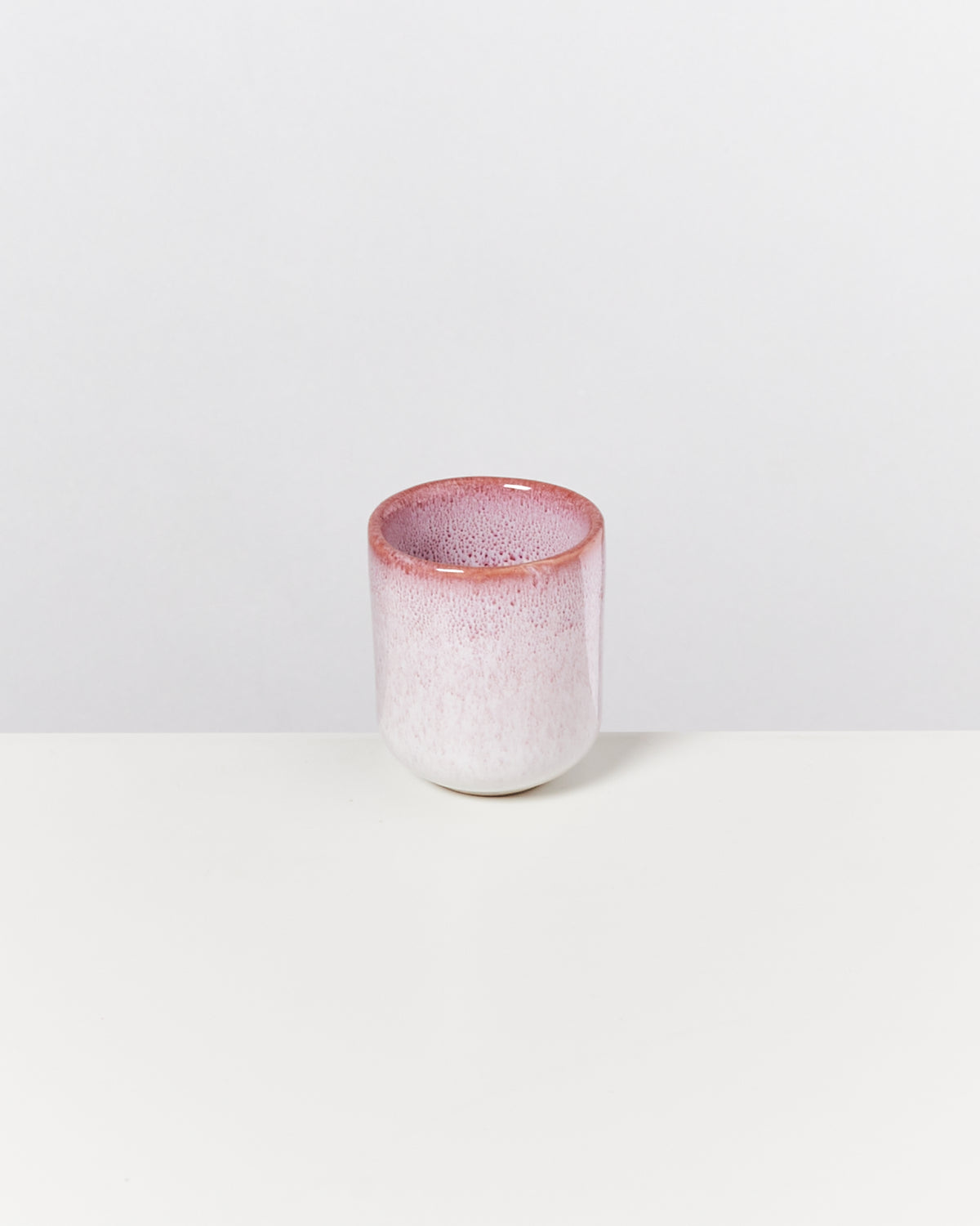 Ein rosa-weißer Keramikbecher steht auf einem weißen Hintergrund.