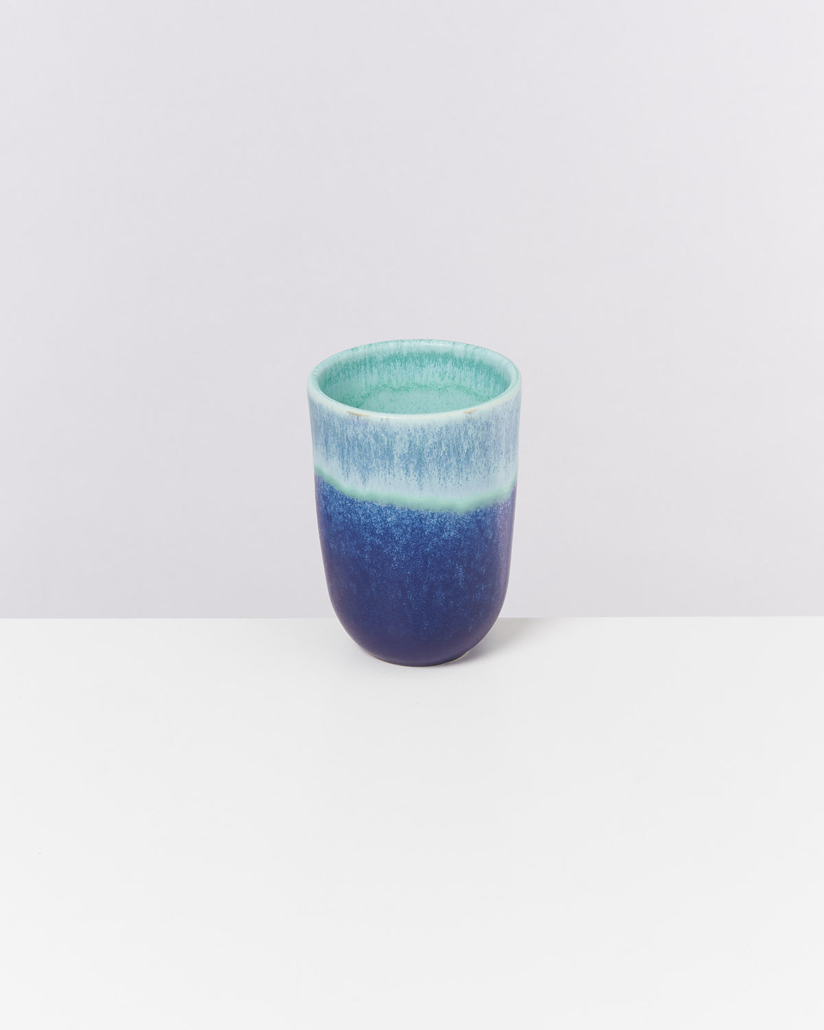 Blauer und mintgrüner Becher auf einem weißen Tisch vor einem grauen Hintergrund.
