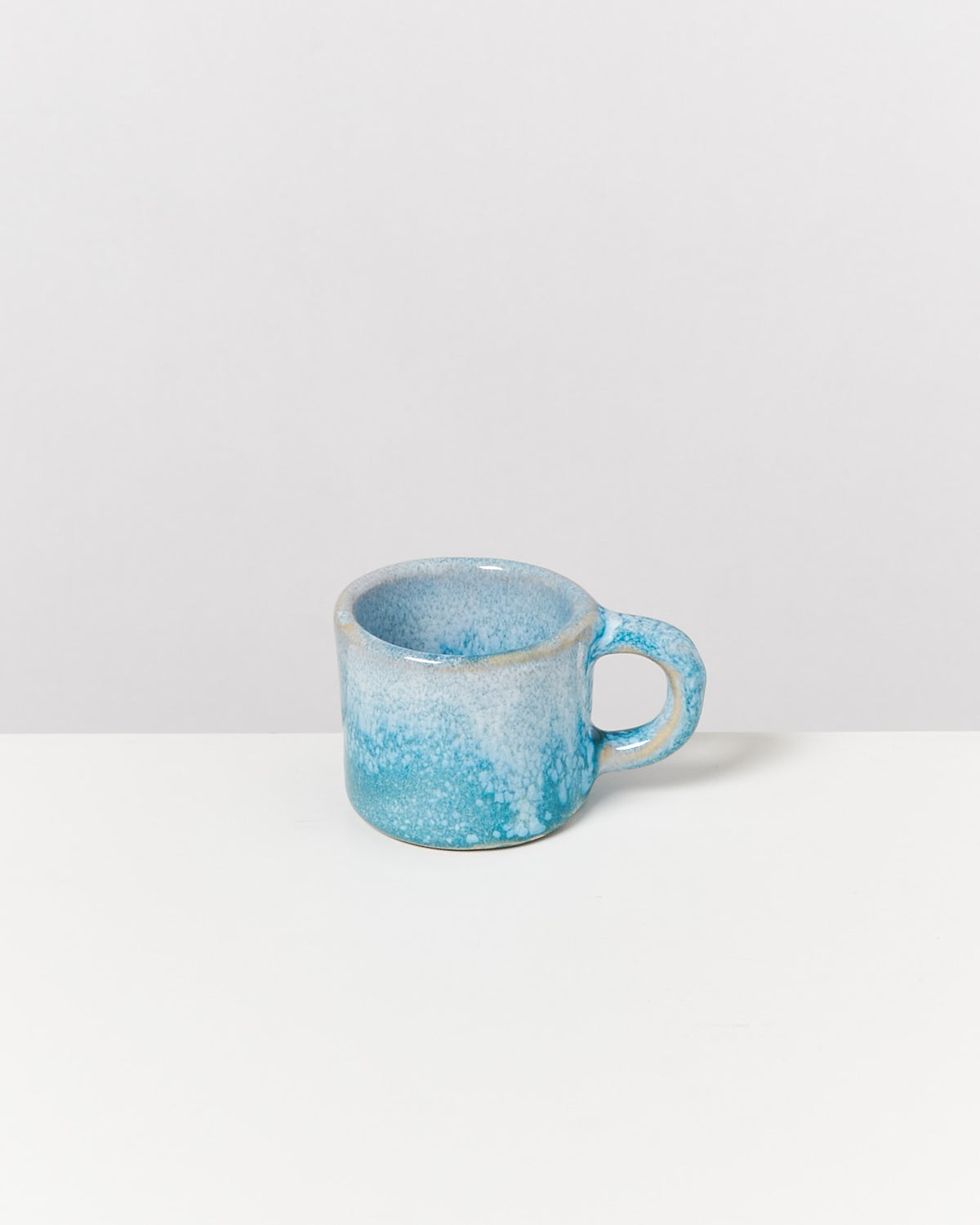 Blaue Keramiktasse mit Sprenkelmuster auf weißem Hintergrund.