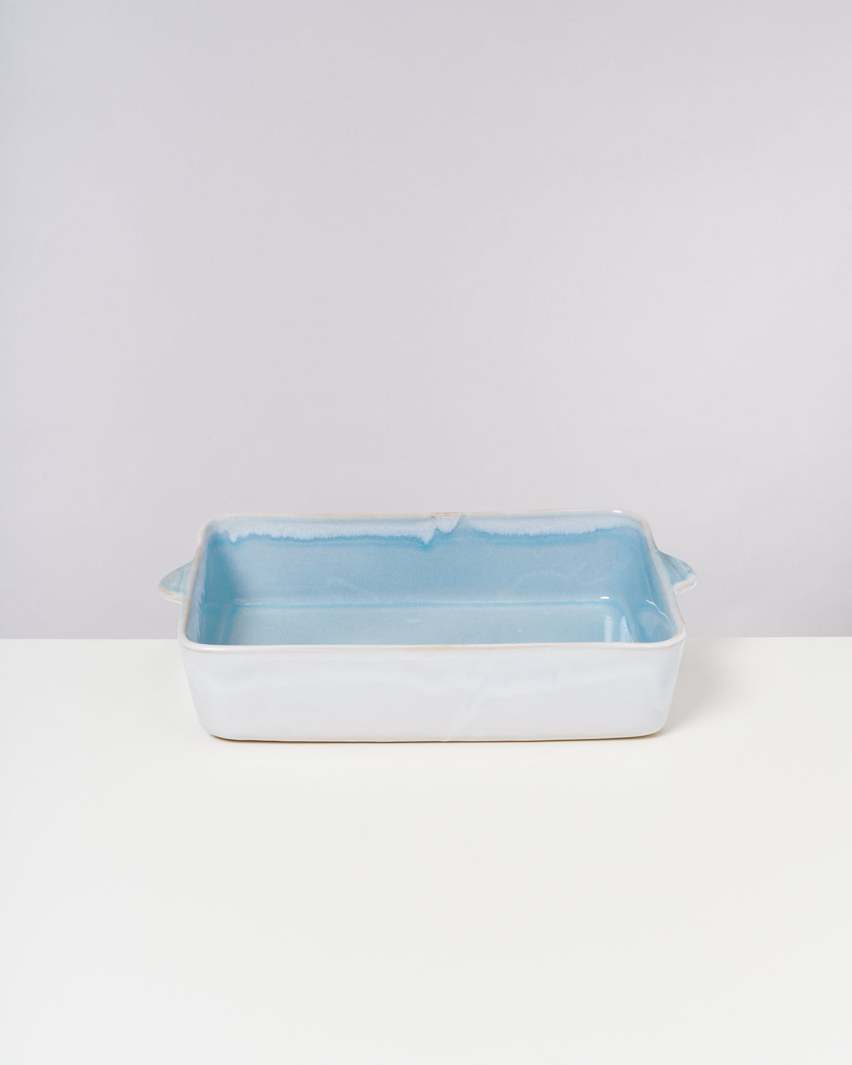 Rechteckige Keramik-Auflaufform mit blauer Innenseite steht auf einem weißen Tisch vor grauem Hintergrund.