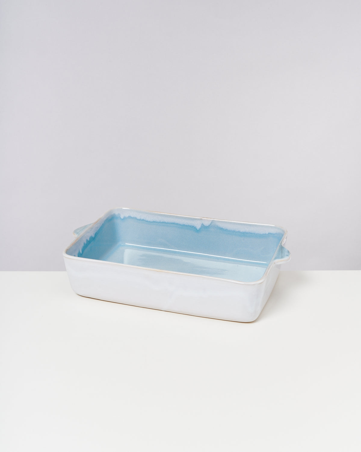 Rechteckige, flache Keramikauflaufform mit blauer Innenseite auf einem weißen Tisch vor grauem Hintergrund.
