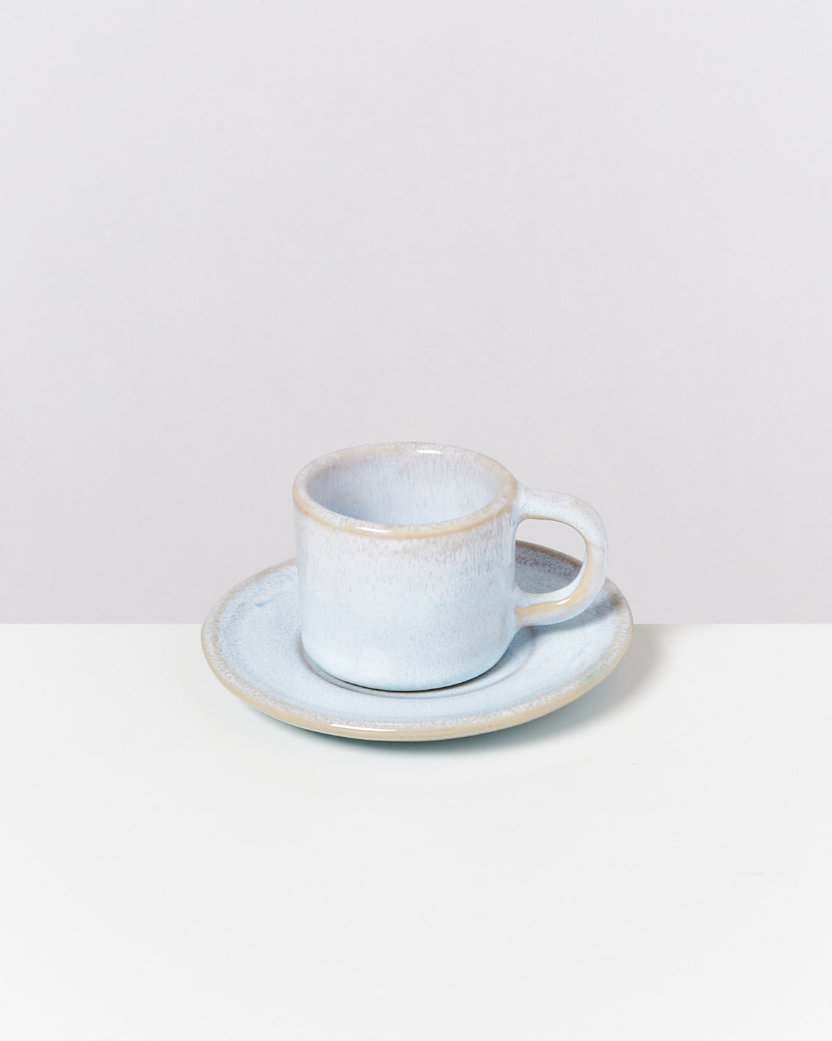 Graue Keramiktasse mit Untertasse auf einem weißen Tisch vor einem grauen Hintergrund.