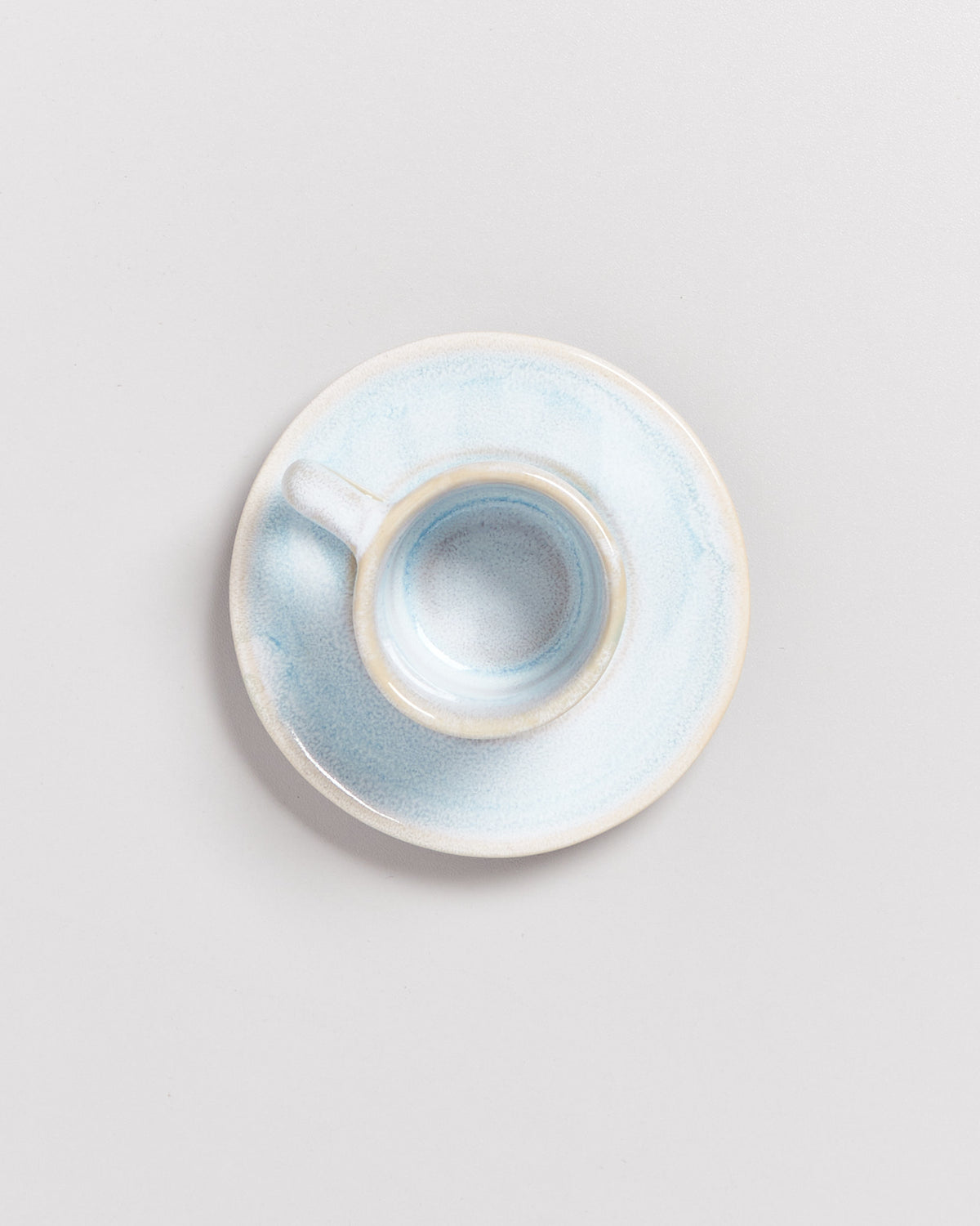 Obenansicht einer leeren Tasse aus Keramik in pastellblau mit passender Untertasse auf einer hellgrauen Oberfläche.