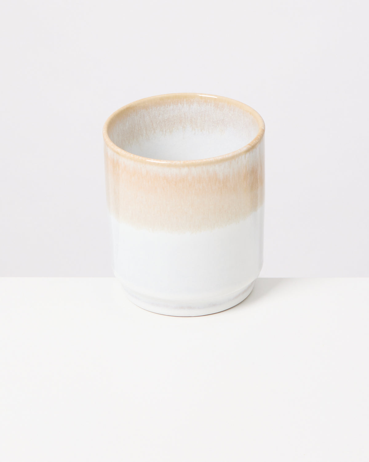 Keramikbecher mit weißem und beigem Farbverlauf auf einem weißen Hintergrund.