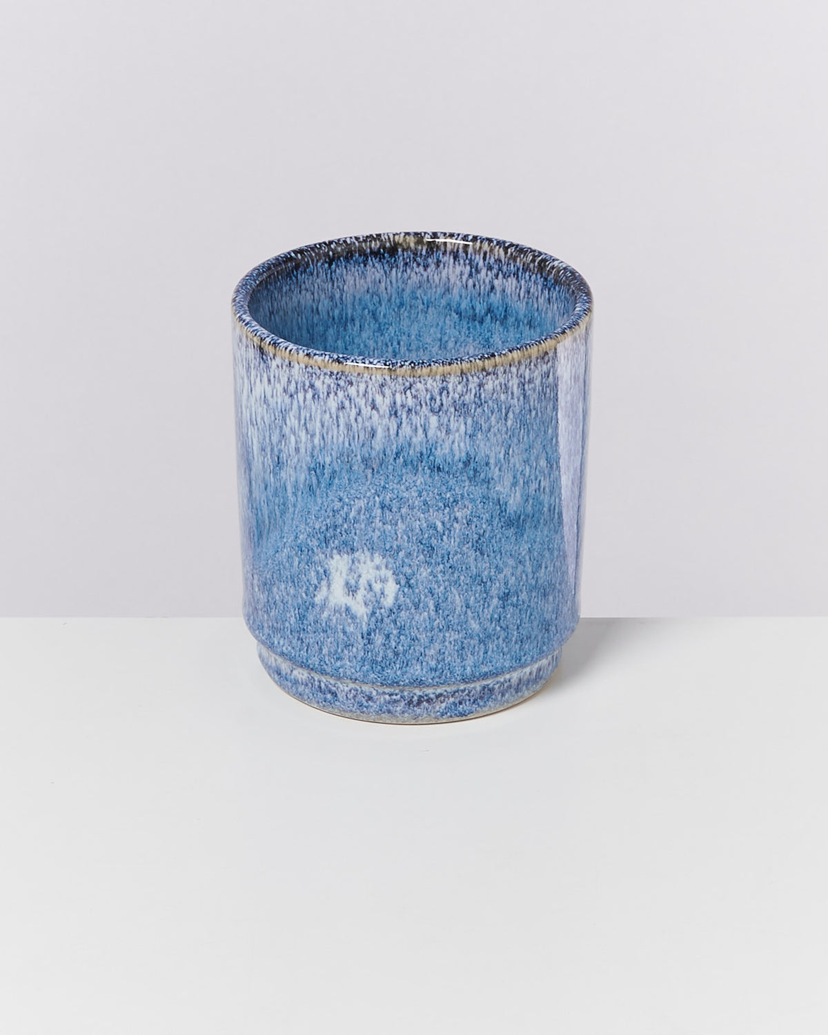 Blaue zylindrische Keramikvase mit gesprenkeltem Muster auf weißem Hintergrund.