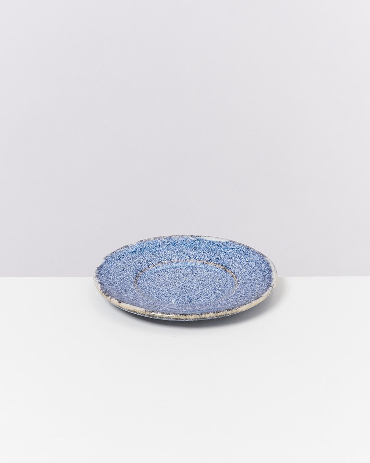 Blauer, texturierter Keramikteller auf weißem Hintergrund, minimalistisches Design.