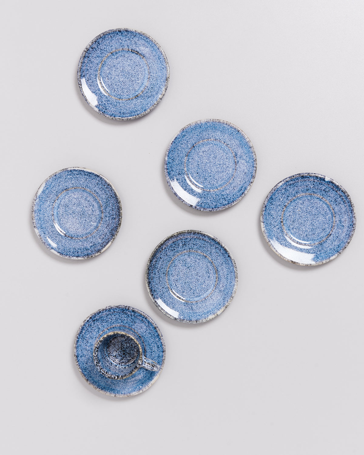 Sechs blaue Keramikteller, einer mit einer Tasse, sind kunstvoll auf einer hellen Oberfläche arrangiert.