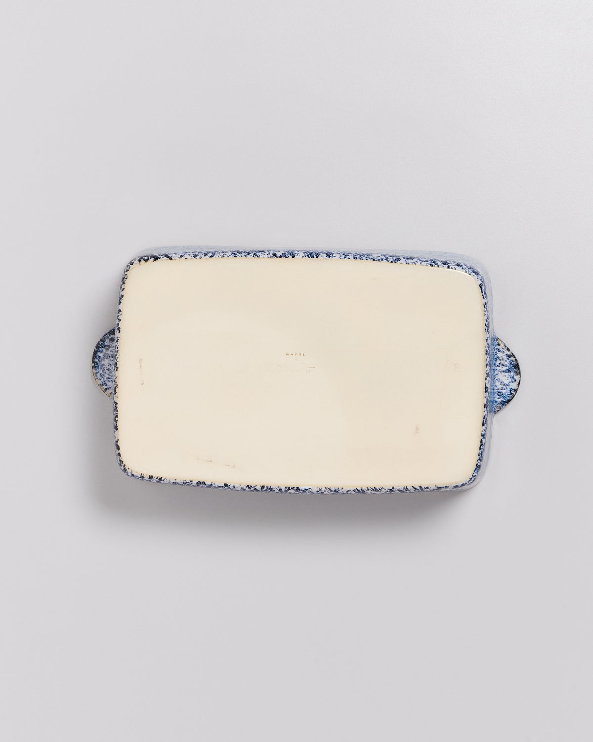 Rechteckige, cremefarbene Keramikplatte mit blaugeflecktem Rand und seitlichen Griffen, auf grauem Hintergrund.