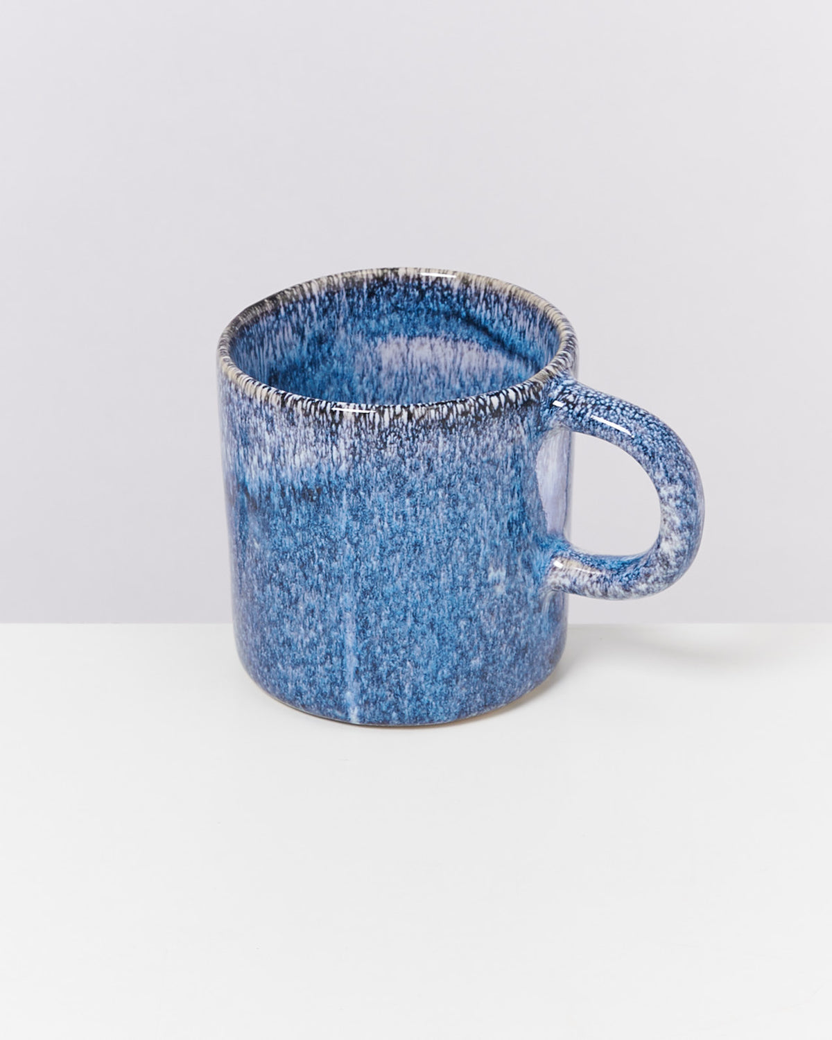 Blaue Keramiktasse mit gräulicher Textur auf einem weißen Hintergrund.