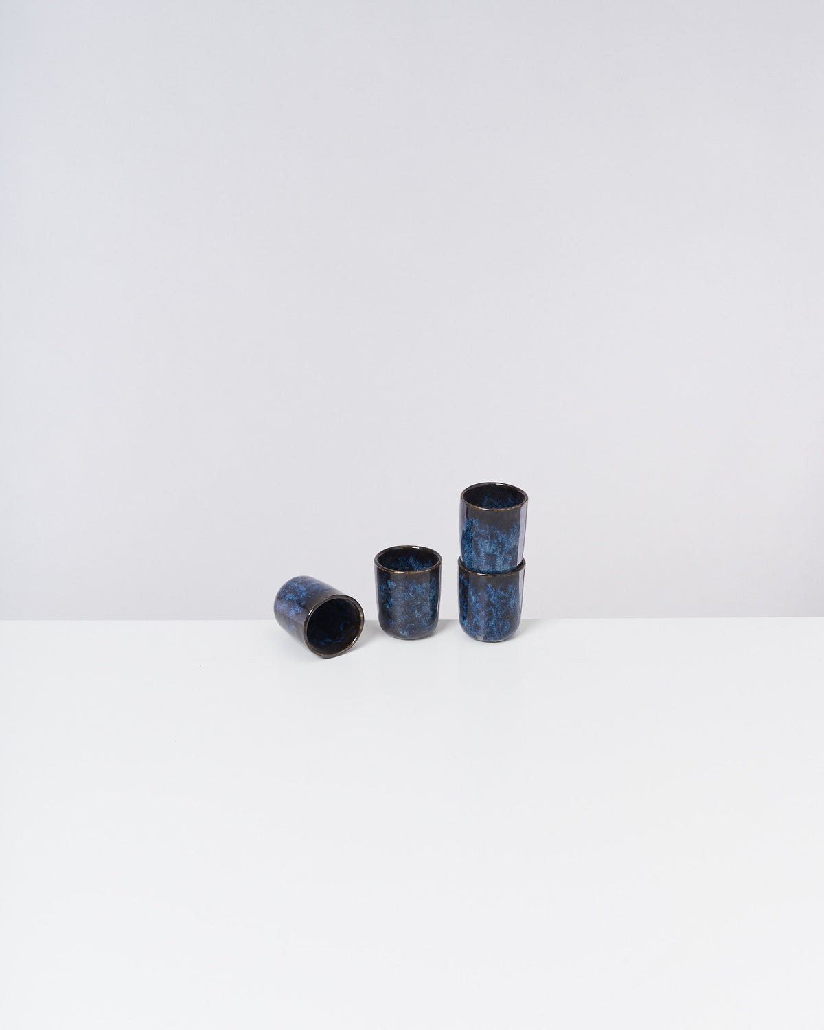 Vier dunkelblaue, stapelbare Keramikbecher auf weißem Hintergrund, einer davon liegt umgekippt.