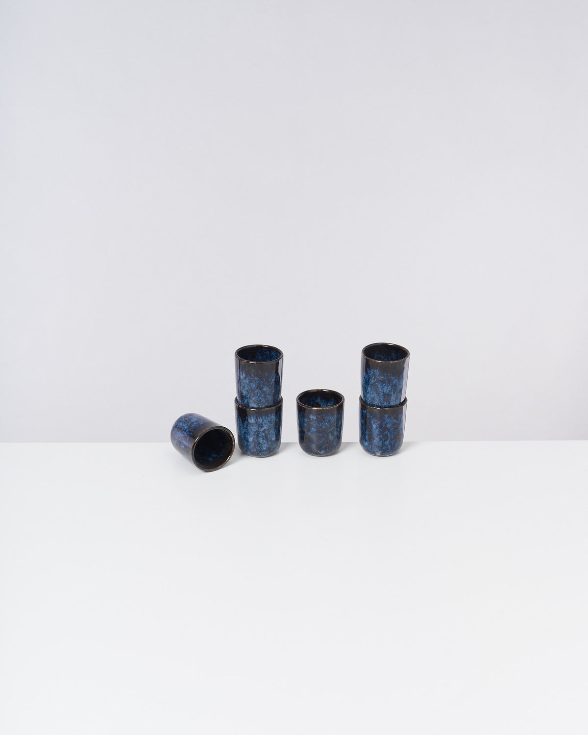 Sechs blaue Becher in zwei gestapelten Gruppen und ein umgekippter Becher auf einem weißen Tisch.