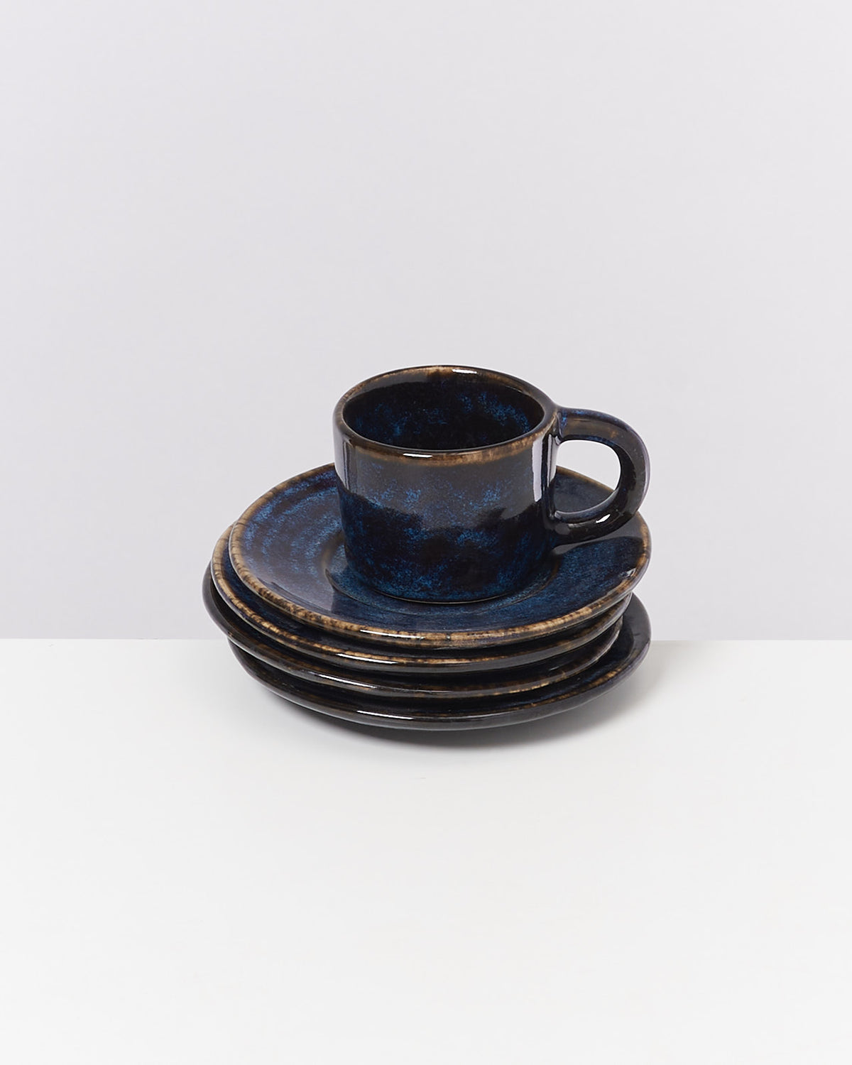Dunkelblaue Tasse mit Untertasse auf gestapelten Tellern, vor neutralem Hintergrund.