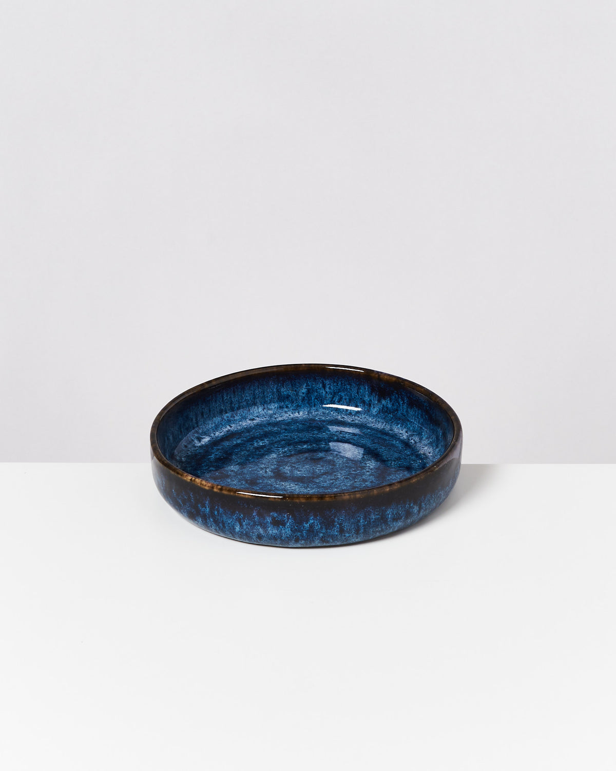 Runde, blaue Keramikschale mit dunklen Rändern auf weißem Hintergrund.